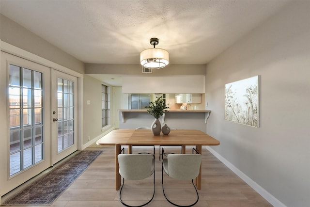 dining room with light wood-type flooring, french doors, baseboards, and a textured ceiling