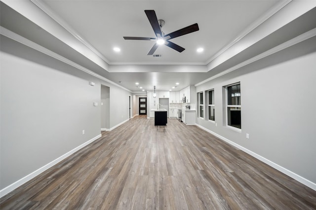 unfurnished living room featuring a tray ceiling, crown molding, recessed lighting, wood finished floors, and baseboards