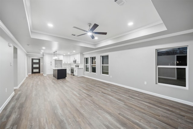 unfurnished living room with visible vents, wood finished floors, a tray ceiling, crown molding, and a sink