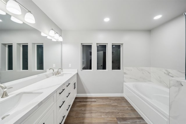 full bath featuring a garden tub, double vanity, wood finished floors, and a sink