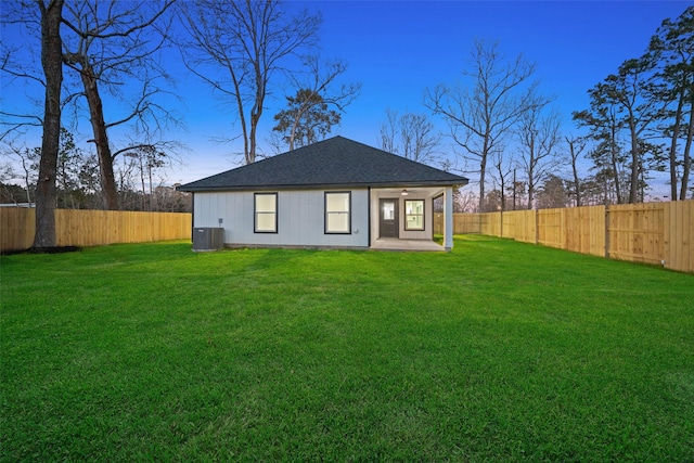 back of property with a fenced backyard, a yard, and central air condition unit