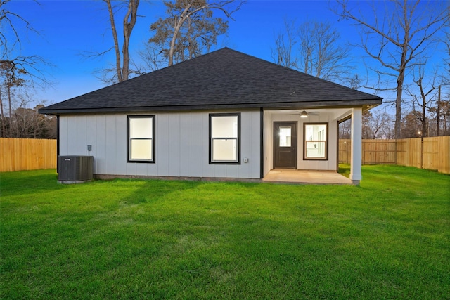 rear view of property with a shingled roof, cooling unit, a fenced backyard, and a yard