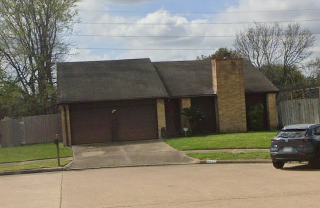 view of front facade with a front yard, driveway, an attached garage, and fence