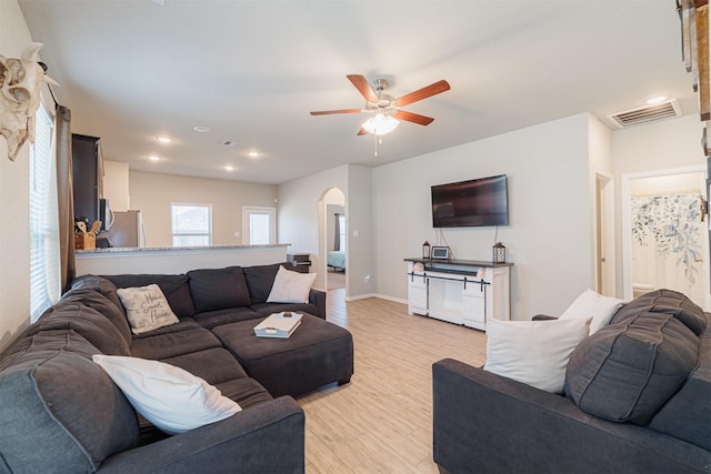 living room featuring light wood finished floors, visible vents, arched walkways, and baseboards