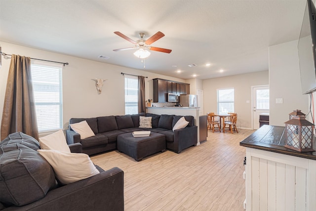 living area with a ceiling fan, a wealth of natural light, visible vents, and light wood finished floors