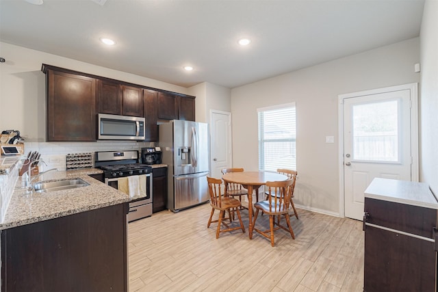 kitchen featuring dark brown cabinetry, light wood finished floors, decorative backsplash, stainless steel appliances, and a sink