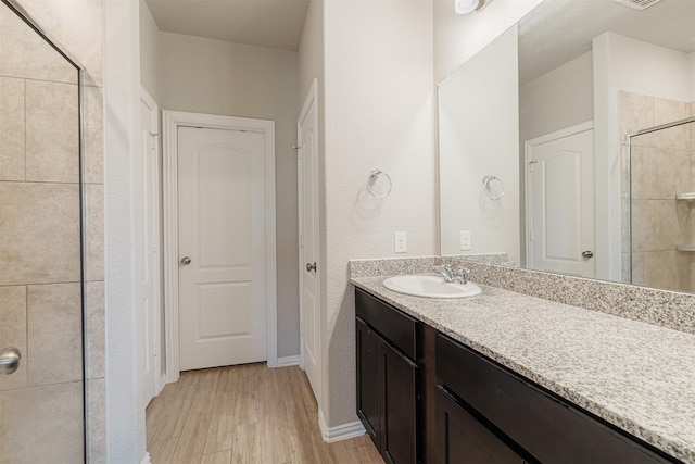 full bathroom featuring wood finished floors, a tile shower, and vanity