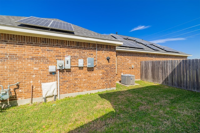 view of property exterior featuring central AC, brick siding, a shingled roof, fence, and a yard