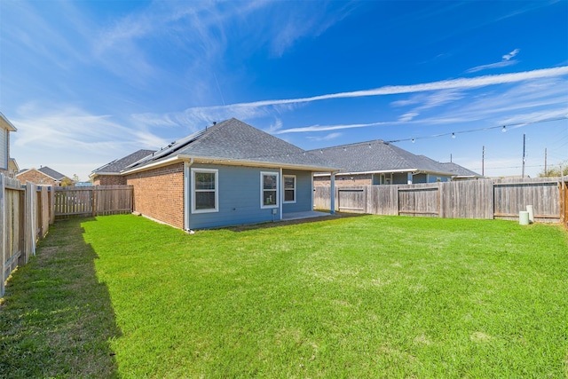 back of house with a shingled roof, solar panels, a fenced backyard, a yard, and brick siding