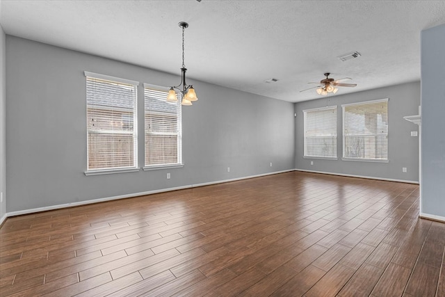 spare room with visible vents, a textured ceiling, wood finished floors, baseboards, and ceiling fan with notable chandelier