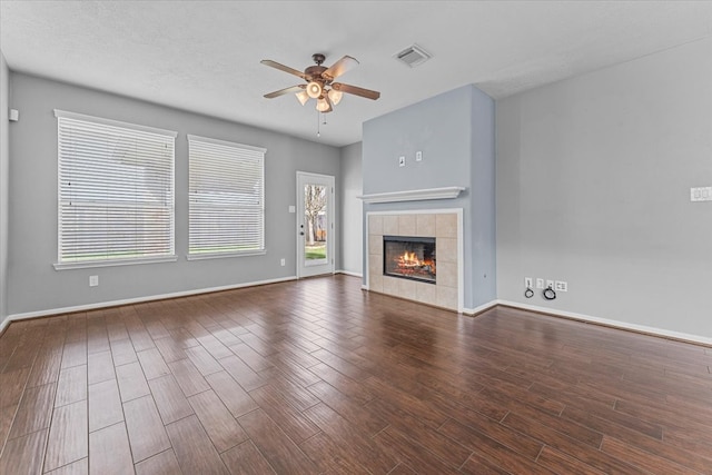 unfurnished living room with baseboards, visible vents, wood finished floors, and a tile fireplace