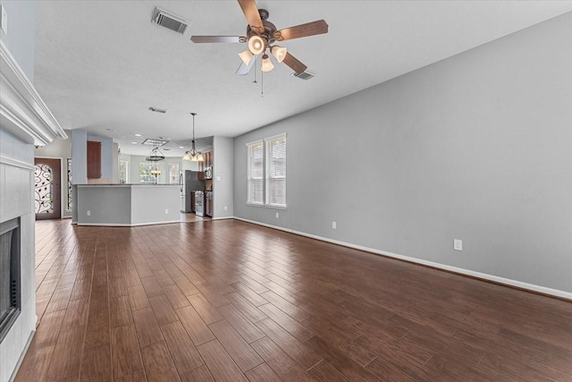 unfurnished living room with baseboards, visible vents, ceiling fan, dark wood-type flooring, and a fireplace