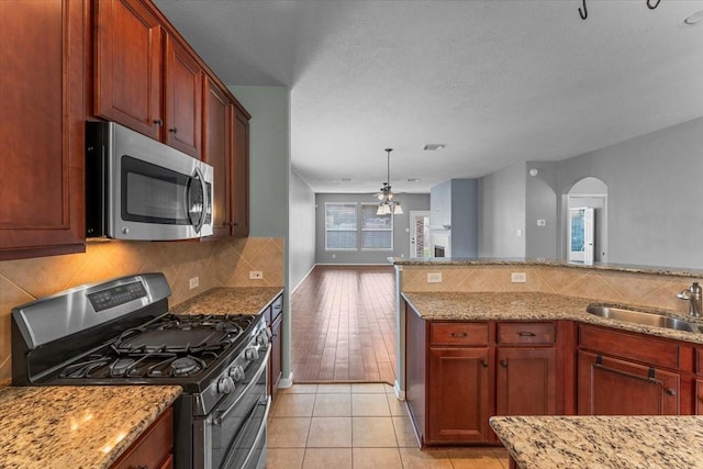 kitchen featuring arched walkways, stainless steel appliances, tasteful backsplash, a sink, and light stone countertops