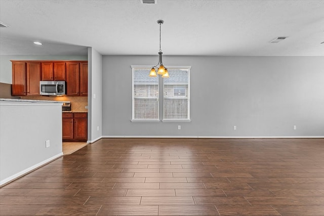 unfurnished living room featuring dark wood-type flooring, visible vents, a notable chandelier, and baseboards