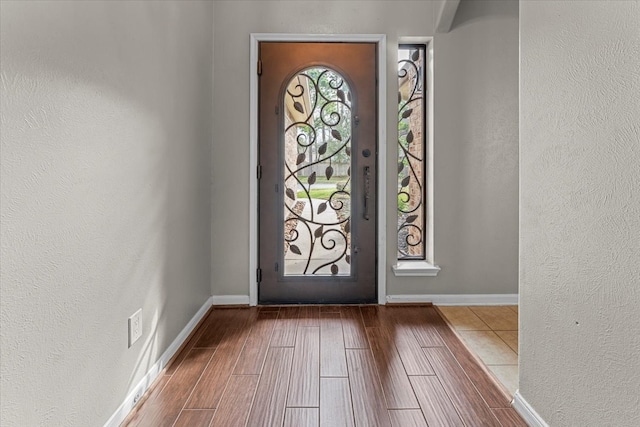 foyer featuring baseboards, wood finished floors, and a textured wall