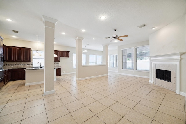 living room with light tile patterned floors, visible vents, a ceiling fan, a tiled fireplace, and decorative columns