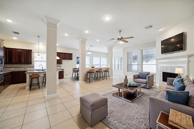 living room featuring visible vents, a tiled fireplace, light tile patterned flooring, ornate columns, and recessed lighting