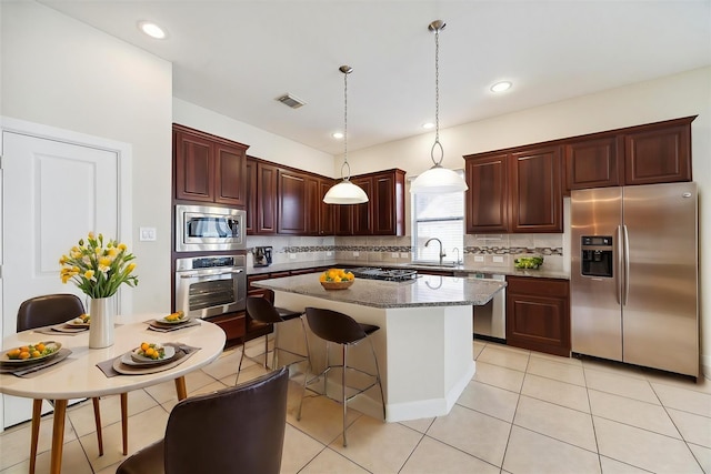 kitchen with stainless steel appliances, a kitchen island, a sink, visible vents, and tasteful backsplash