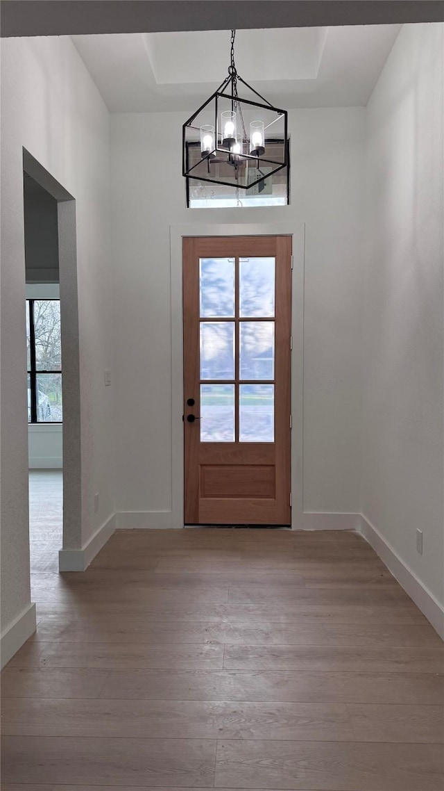 doorway with an inviting chandelier, plenty of natural light, baseboards, and light wood-style flooring