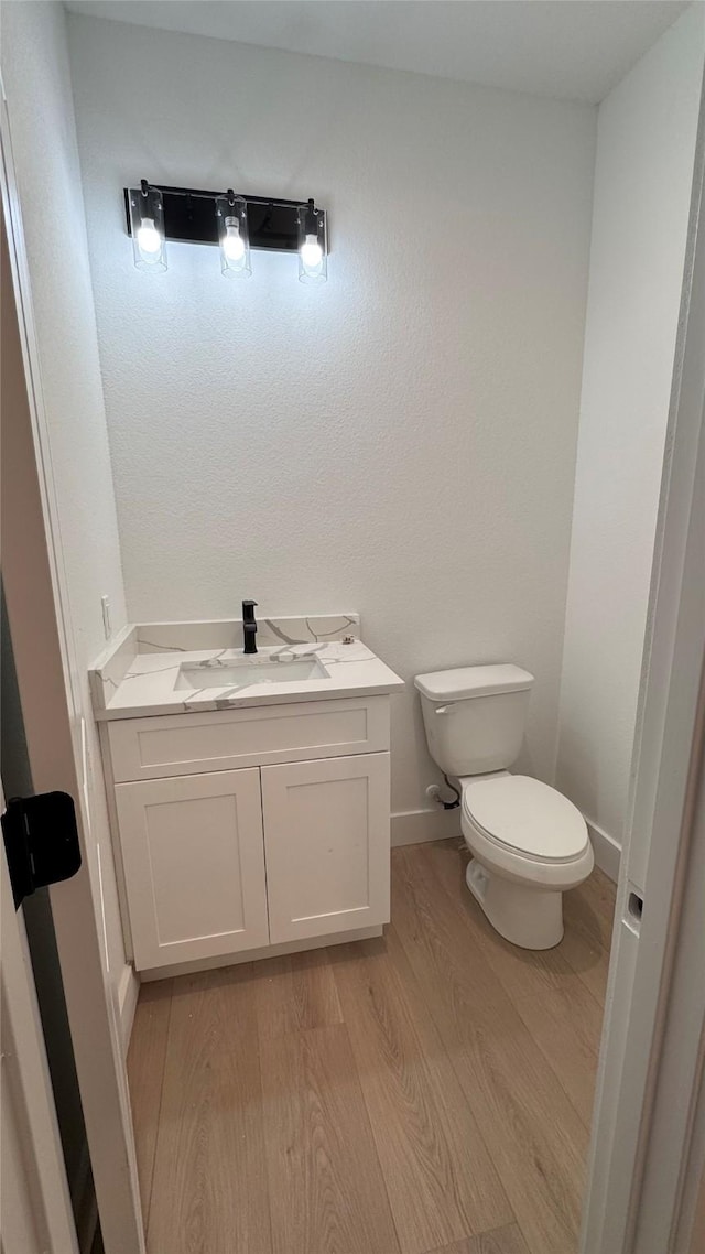 half bath with baseboards, vanity, toilet, and wood finished floors