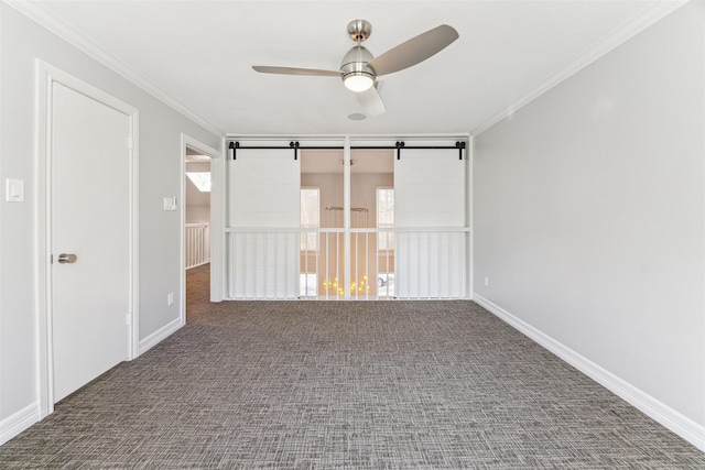 carpeted spare room with ceiling fan, a barn door, baseboards, and crown molding