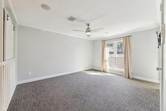 carpeted spare room featuring visible vents, a barn door, a ceiling fan, ornamental molding, and baseboards