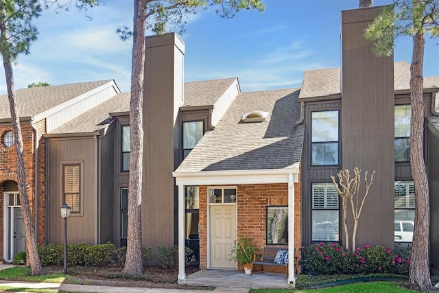 multi unit property with a shingled roof, a chimney, and brick siding