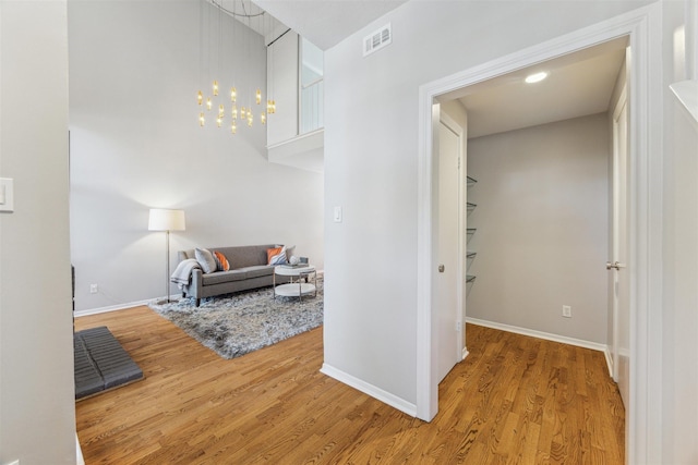 corridor with a chandelier, wood finished floors, visible vents, and baseboards