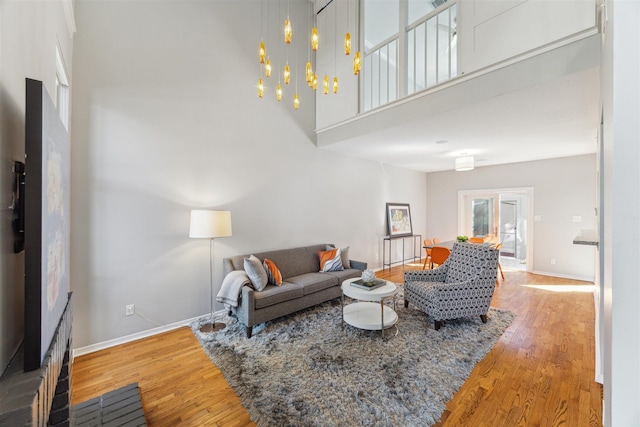 living area with an inviting chandelier, a towering ceiling, baseboards, and wood finished floors