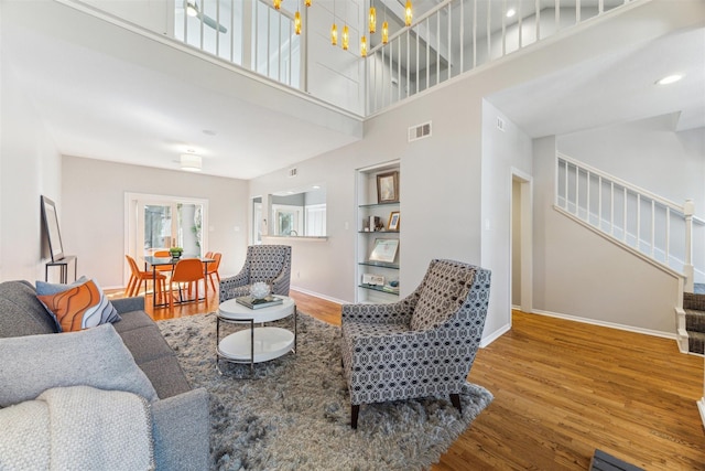 living area with stairs, wood finished floors, visible vents, and baseboards