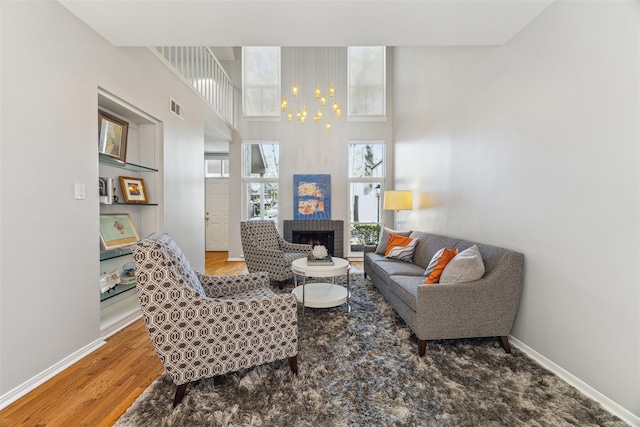 living room with a fireplace, visible vents, a high ceiling, wood finished floors, and baseboards