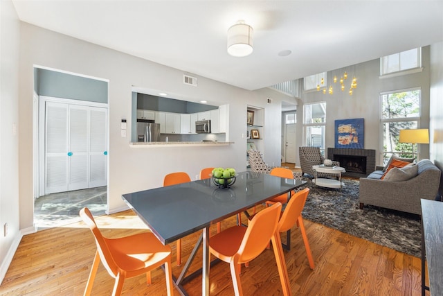 dining area featuring a brick fireplace, visible vents, light wood-style flooring, and baseboards