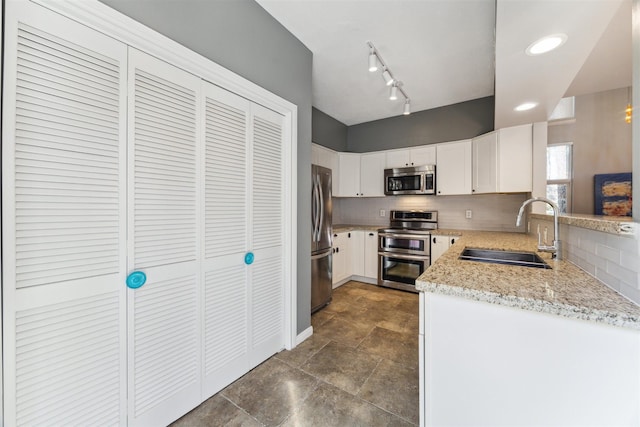 kitchen featuring light stone counters, stainless steel appliances, decorative backsplash, white cabinets, and a sink