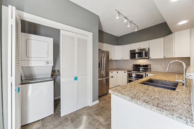 kitchen with stacked washer / dryer, a sink, appliances with stainless steel finishes, decorative backsplash, and light stone countertops