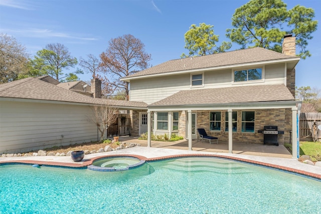 rear view of property with brick siding, fence, a pool with connected hot tub, a chimney, and a patio area