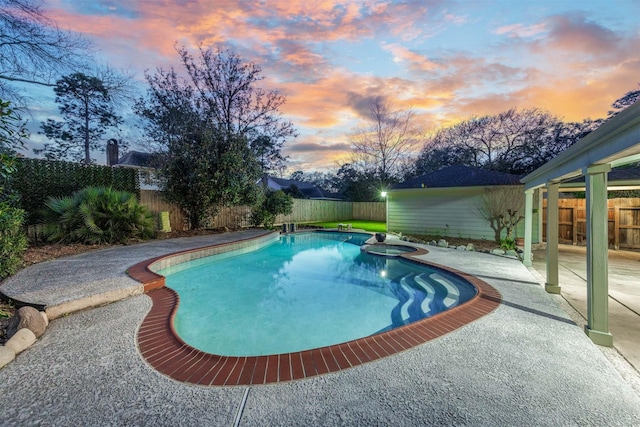 pool at dusk featuring a pool with connected hot tub, a patio area, and a fenced backyard