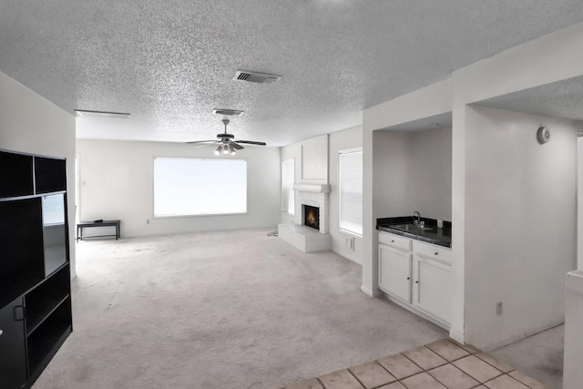 unfurnished living room with visible vents, light colored carpet, a fireplace, a ceiling fan, and a sink