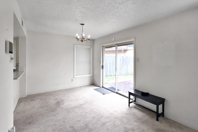 carpeted empty room with a notable chandelier, visible vents, a textured ceiling, and baseboards