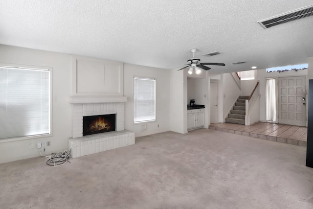 unfurnished living room with stairs, a brick fireplace, light colored carpet, and visible vents