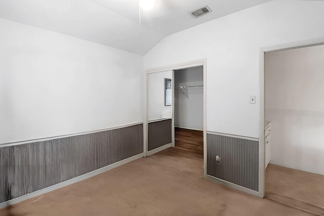 unfurnished bedroom featuring a closet, visible vents, wainscoting, and vaulted ceiling