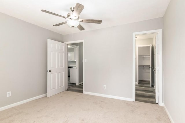 unfurnished bedroom with a closet, light colored carpet, a walk in closet, and baseboards