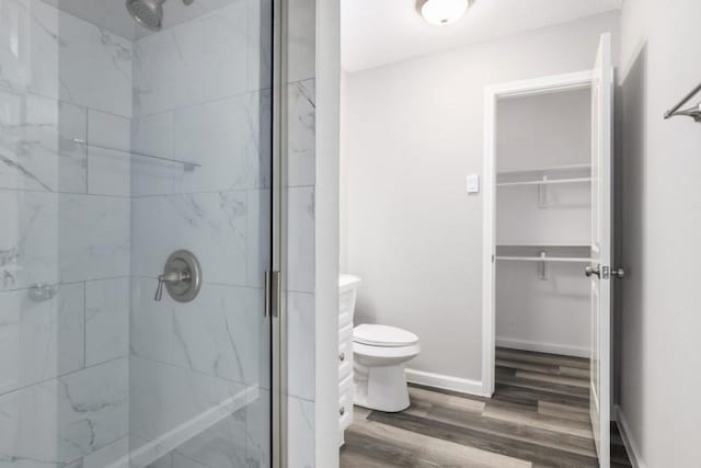 full bath featuring toilet, wood finished floors, a shower stall, baseboards, and a spacious closet