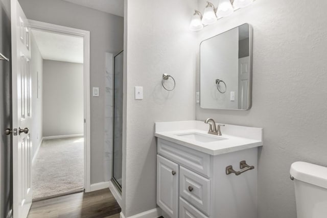 bathroom with an enclosed shower, toilet, wood finished floors, baseboards, and vanity