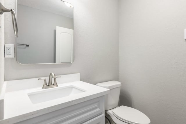 half bathroom with toilet, vanity, and a textured wall