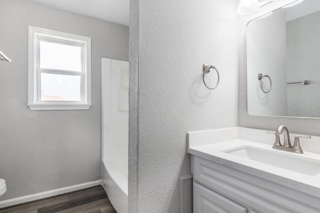 full bathroom featuring vanity, wood finished floors, baseboards, toilet, and a textured wall