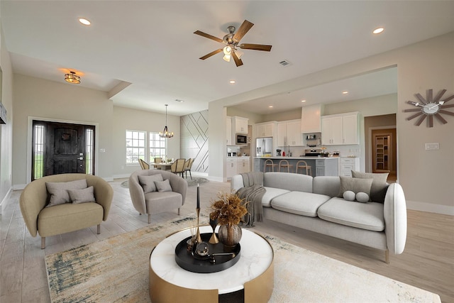 living area with ceiling fan with notable chandelier, light wood finished floors, baseboards, and recessed lighting