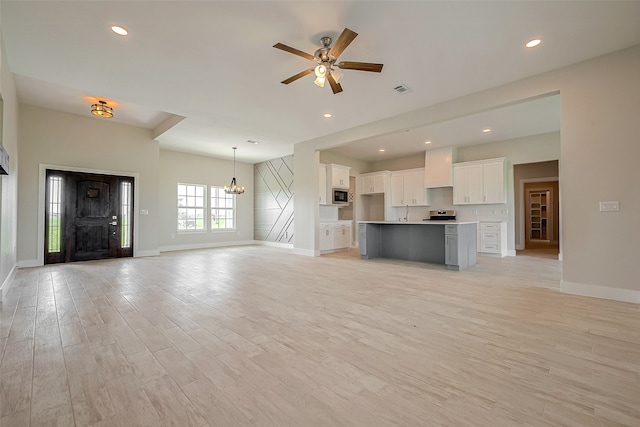 unfurnished living room with light wood-style flooring, baseboards, and ceiling fan with notable chandelier