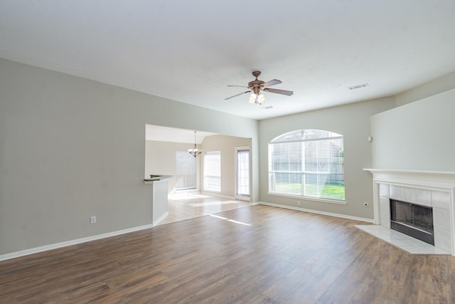 unfurnished living room featuring visible vents, baseboards, wood finished floors, a fireplace, and ceiling fan with notable chandelier