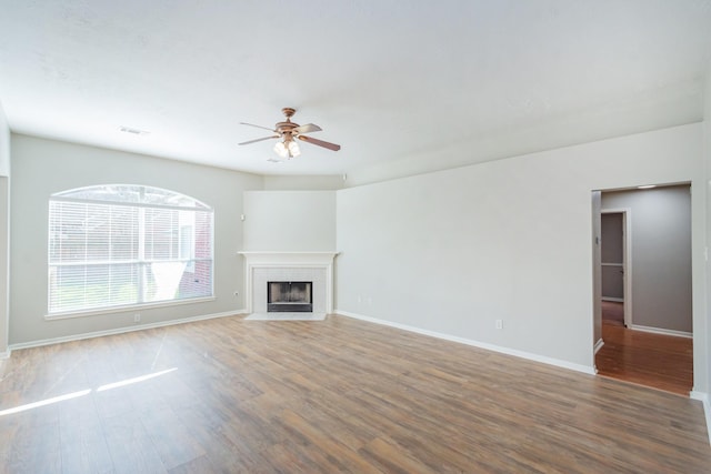 unfurnished living room with baseboards, visible vents, a tiled fireplace, ceiling fan, and wood finished floors