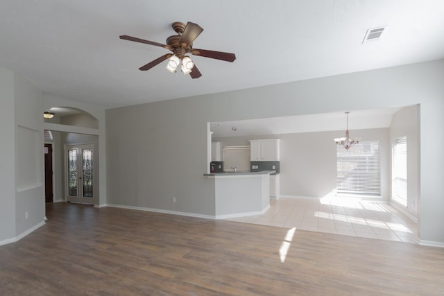 unfurnished living room featuring baseboards, visible vents, light wood finished floors, and ceiling fan with notable chandelier